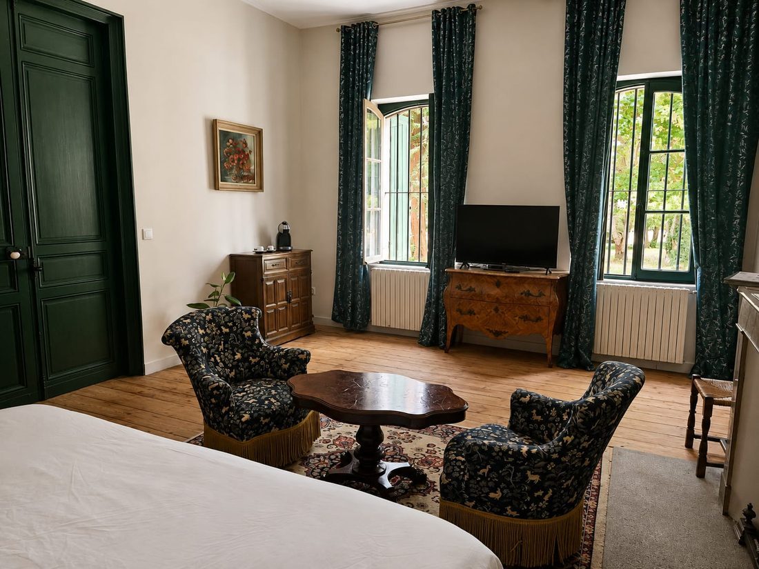 La Grande Chambre Verte — coin salon aux fauteuils à franges, hautes portes-fenêtres vertes ouvertes sur le parc